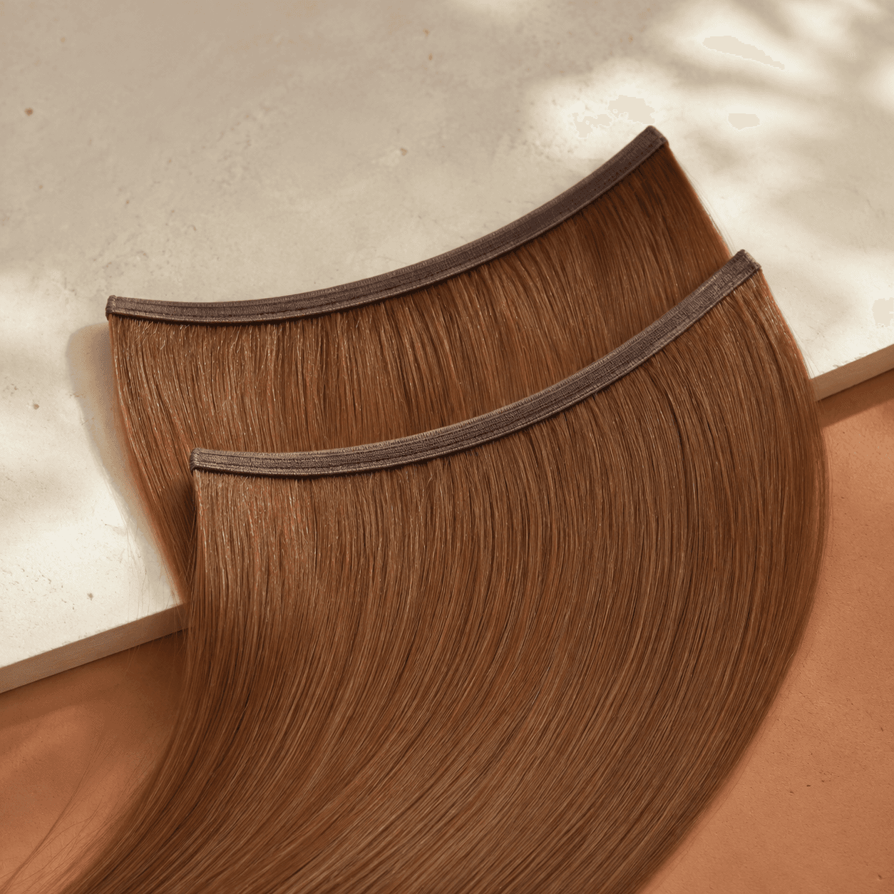 Two caramel-brown flat human hair wefts with thin reinforced seams