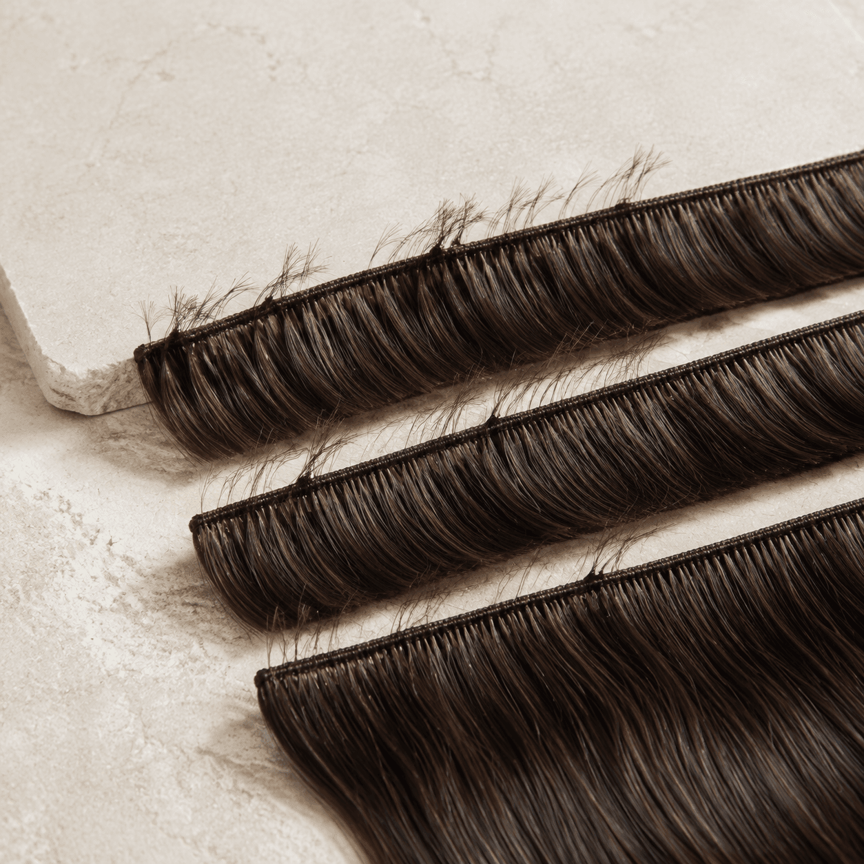 Three dark-brown hand-tied human hair wefts showing narrow stitched tracks